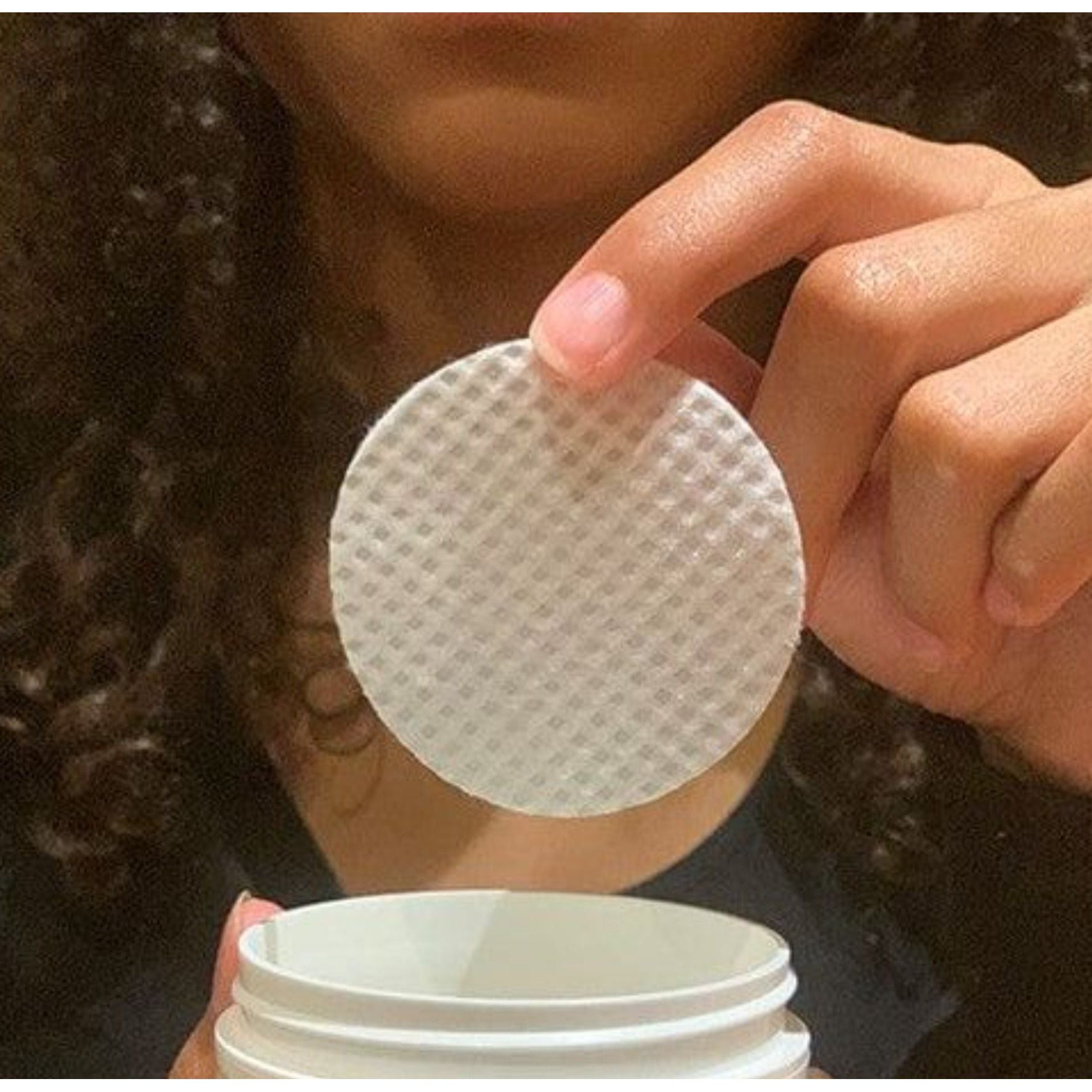 Hand holding up white peel pad over jar